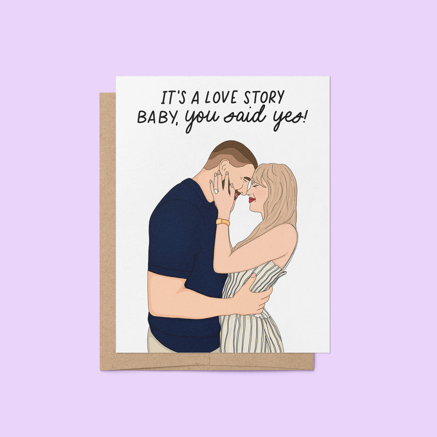Illustrated engagement card featuring a couple embracing with the caption “It’s a love story baby, you said yes!” above them.