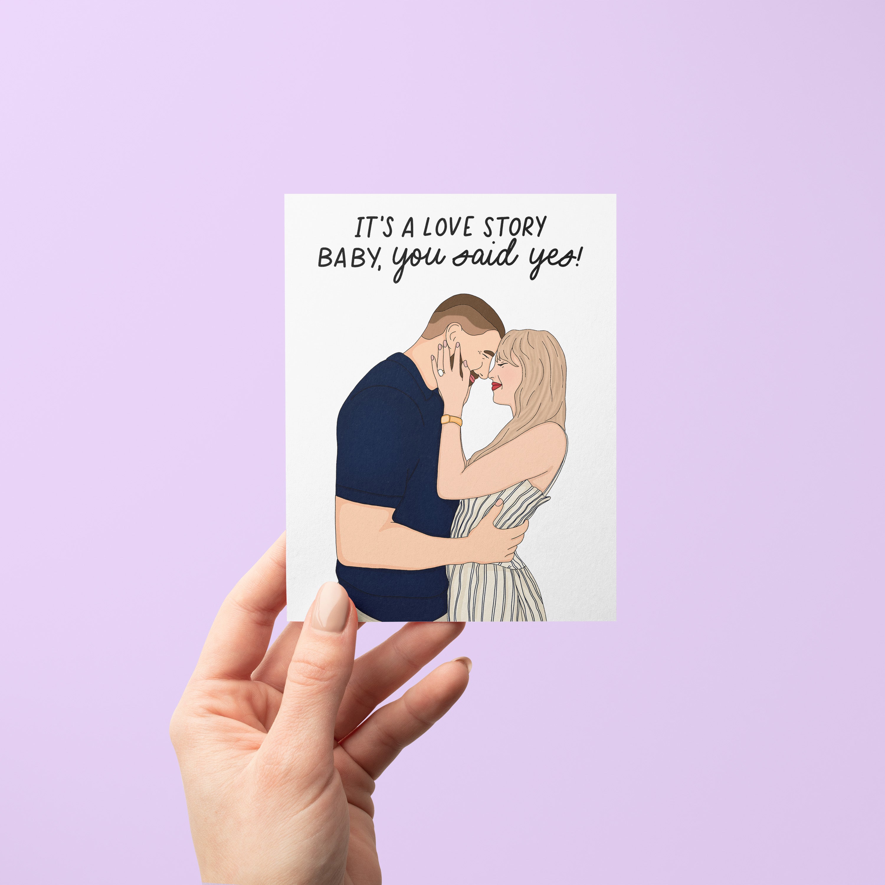 Illustrated engagement card featuring a couple embracing with the caption “It’s a love story baby, you said yes!” above them.