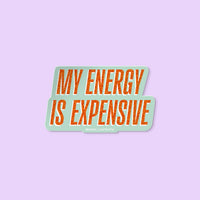 Vinyl sticker with glitter-style orange text reading “My Energy Is Expensive” on a mint background.
