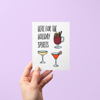 Holiday greeting card with illustrated drinks including mulled wine, champagne, and a martini with candy cane, featuring the phrase "Here For the Holiday Spirits."
