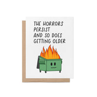 Funny birthday card with illustration of a flaming dumpster and the words “The horrors persist and so does getting older” in bold text, blank inside with kraft envelope.