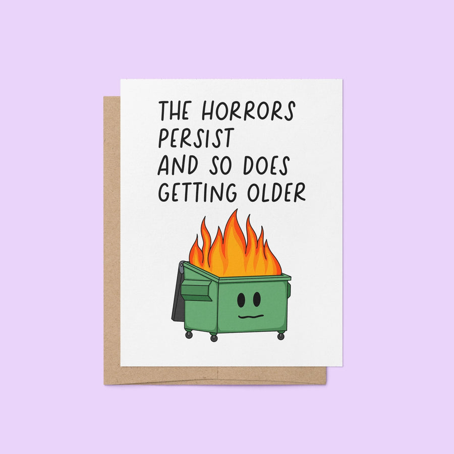 Funny birthday card with illustration of a flaming dumpster and the words “The horrors persist and so does getting older” in bold text, blank inside with kraft envelope.