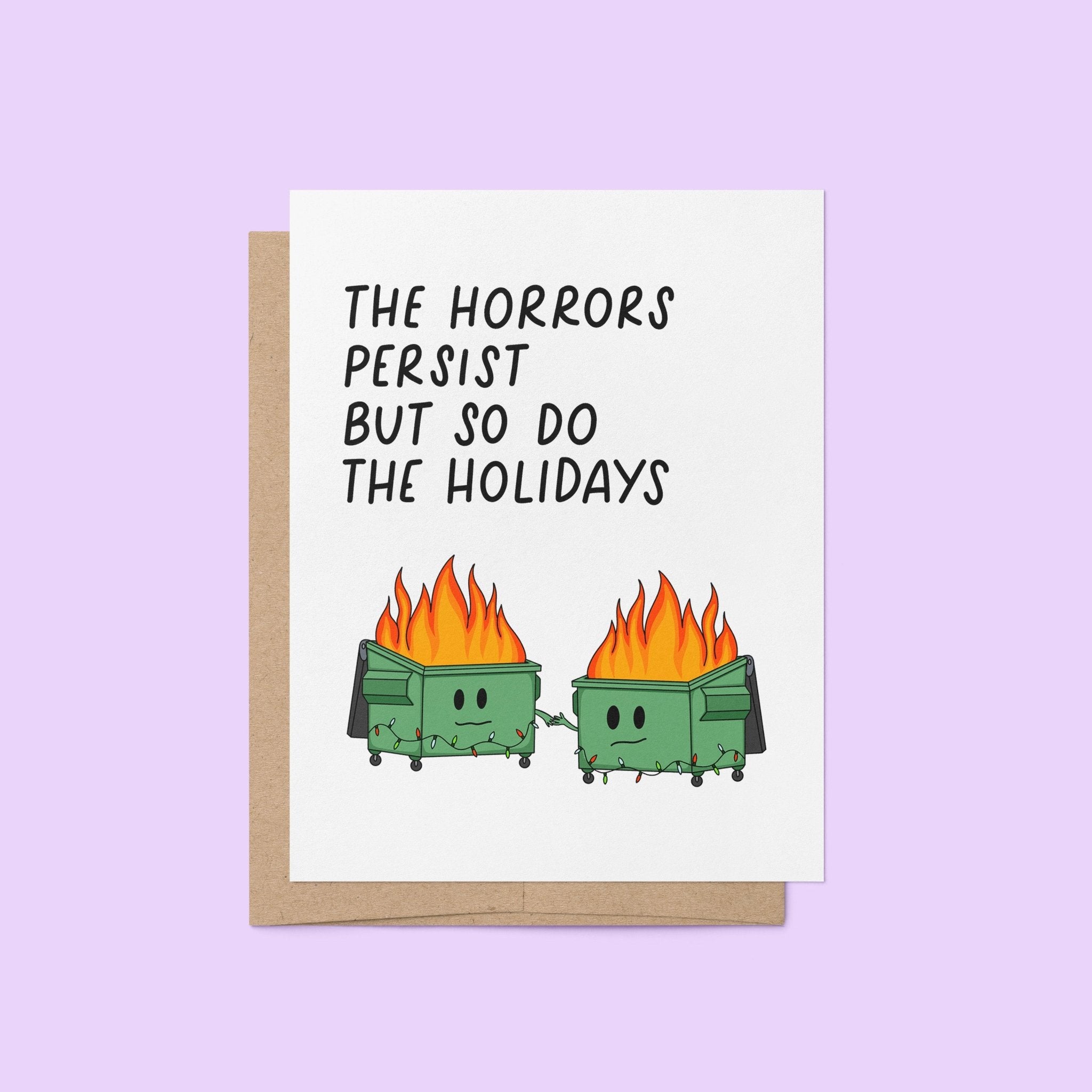 Humorous holiday card with two flaming dumpster characters holding hands, decorated with string lights, and the text “The horrors persist but so do the holidays.”