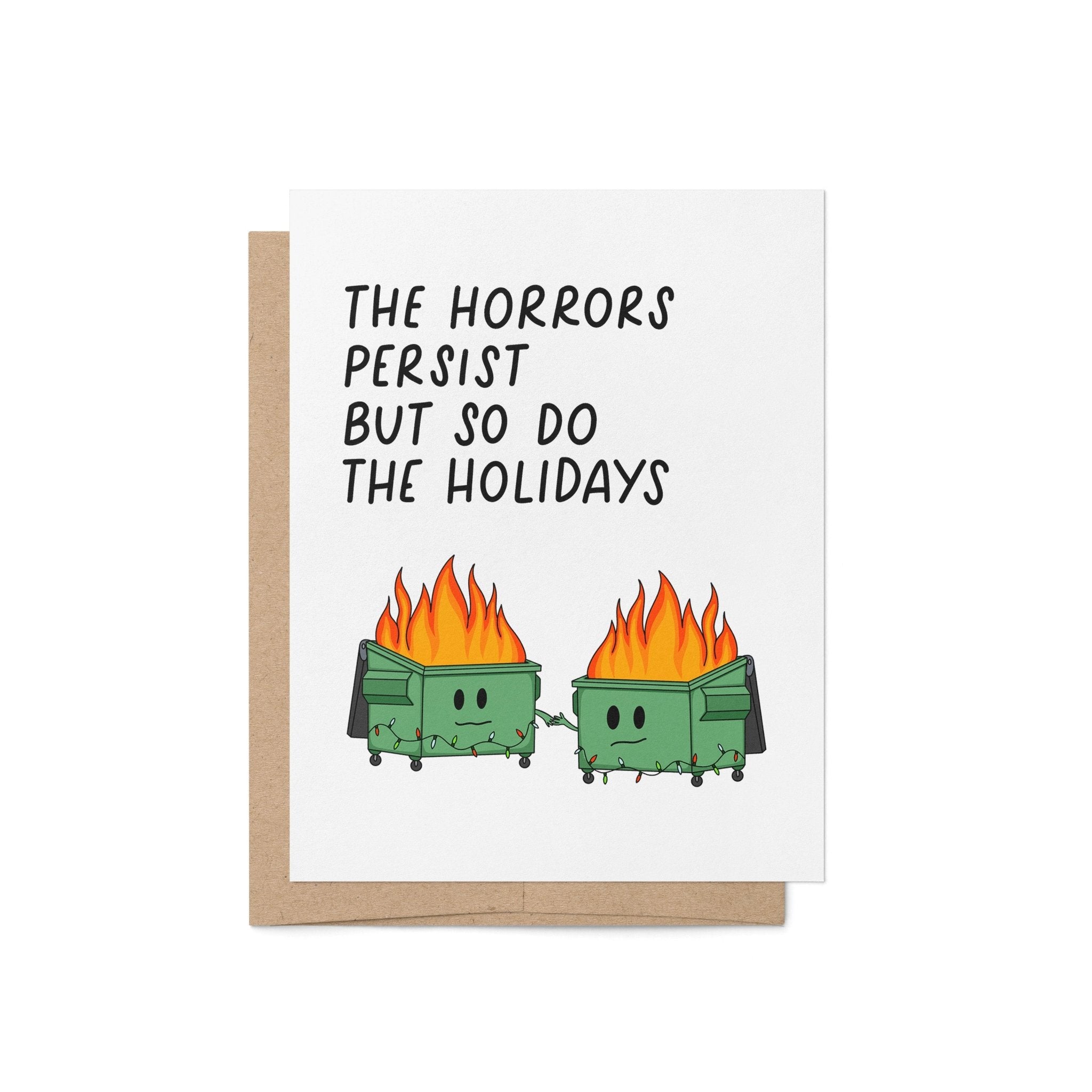 Humorous holiday card with two flaming dumpster characters holding hands, decorated with string lights, and the text “The horrors persist but so do the holidays.”