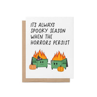 Funny Halloween card with two flaming dumpster illustrations, pumpkins, and the phrase “It’s Always Spooky Season When the Horrors Persist”
