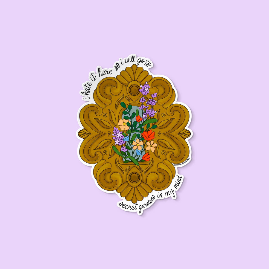 Vinyl sticker with ornate golden frame, blooming flowers, and the text “I hate it here so I will go to secret gardens in my mind.”