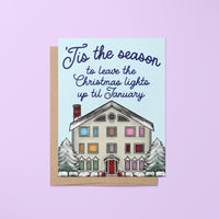 This Swiftie holiday card features an illustration of the Lover House decked out in Christmas lights and dusted with snow. The greeting reads &quot;&#39;Tis the season to leave the Christmas lights up till January.&quot;