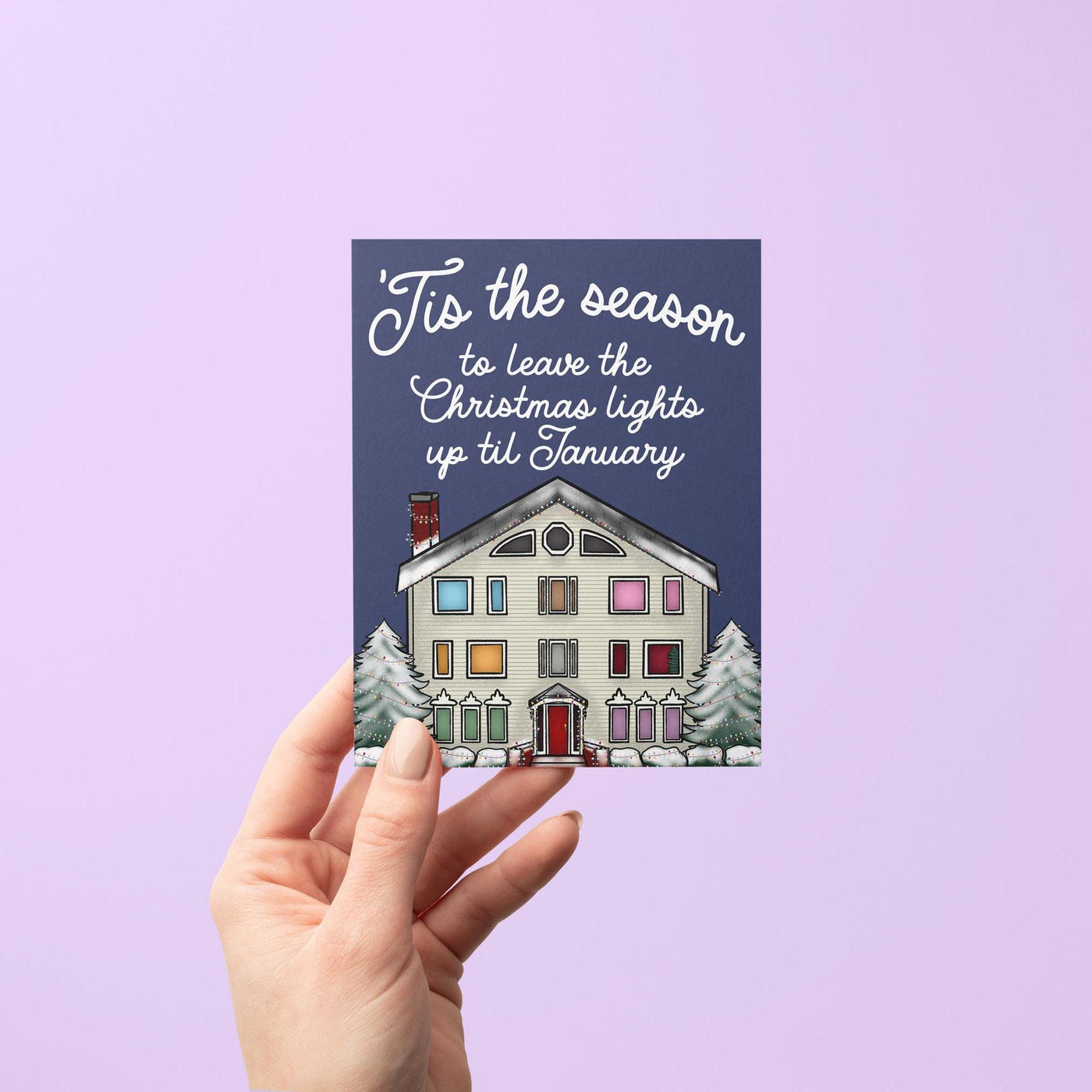 This Swiftie holiday card features an illustration of the Lover House decked out in Christmas lights and dusted with snow. The greeting reads &quot;&#39;Tis the season to leave the Christmas lights up till January.&quot;