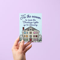 This Swiftie holiday card features an illustration of the Lover House decked out in Christmas lights and dusted with snow. The greeting reads &quot;&#39;Tis the season to leave the Christmas lights up till January.&quot;