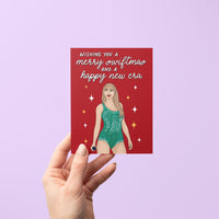 This card features an illustration of Tay in a green version of her Lover era Eras Tour bodysuit surrounded by stars. The greeting in mixed script and sans serif hand lettering reads &quot;wishing you a merry swiftmas and a happy new era.&quot;