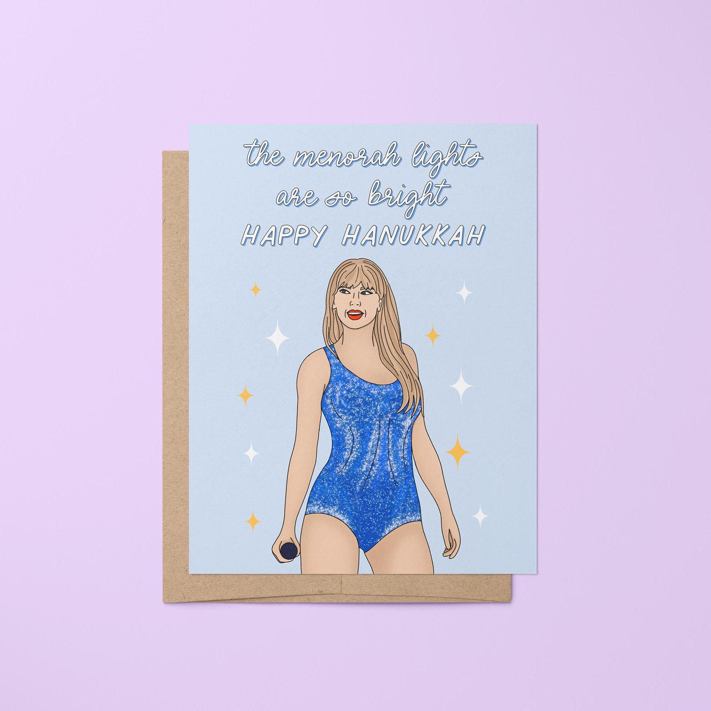 This Swiftie Hanukkah card features an illustration of Tay in a blue version of her Lover era Eras Tour bodysuit surrounded by stars against a light blue background. The greeting reads &quot;the menorah lights are so bright. Happy Hanukkah.&quot;