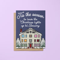 This Swiftie holiday card features an illustration of the Lover House decked out in Christmas lights and dusted with snow. The greeting reads &quot;&#39;Tis the season to leave the Christmas lights up till January.&quot;