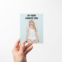 Engagement card with the phrase “In Your Fiancée Era” featuring an illustration of a woman in a sparkling outfit with a bridal veil and microphone.