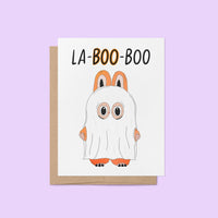 Halloween greeting card with the words “La-BOO-boo” and an illustration of a cute monster in a ghost costume with bunny ears.