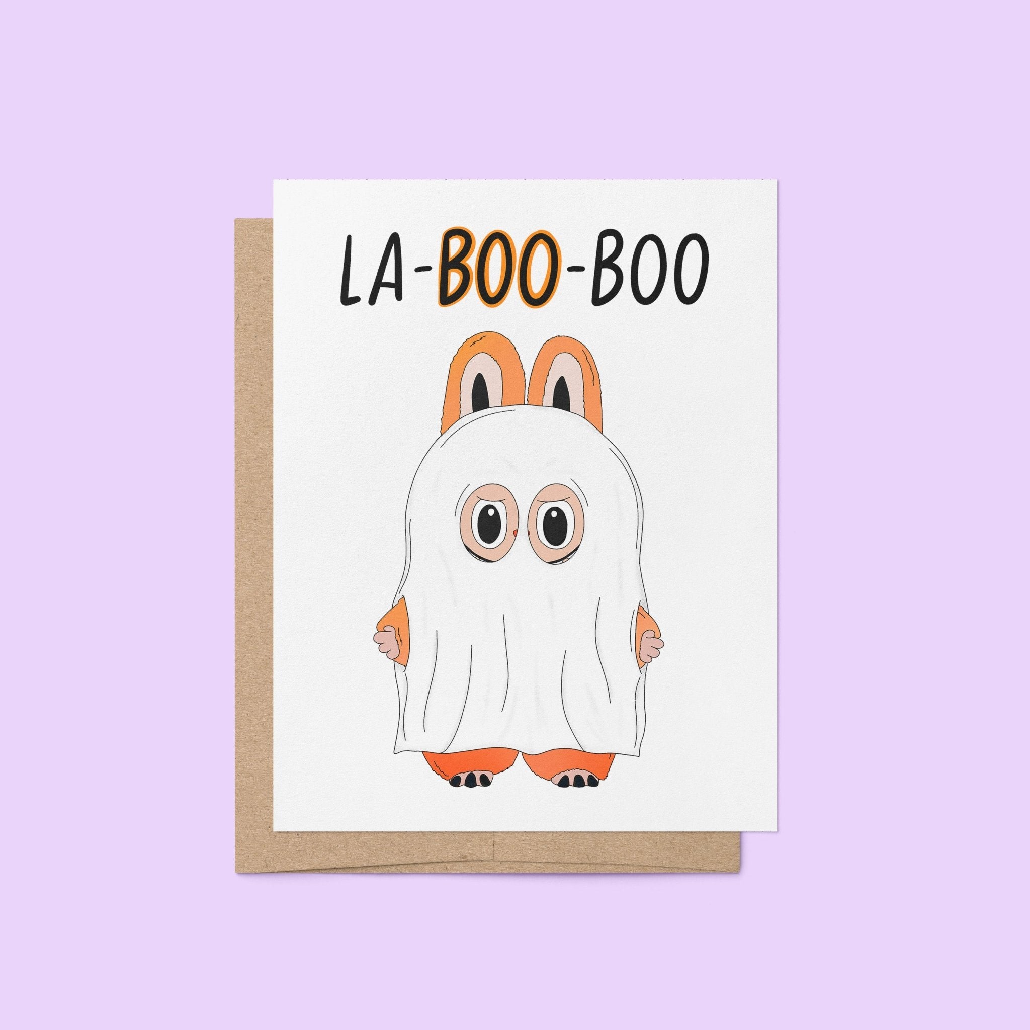 Halloween greeting card with the words “La-BOO-boo” and an illustration of a cute monster in a ghost costume with bunny ears.