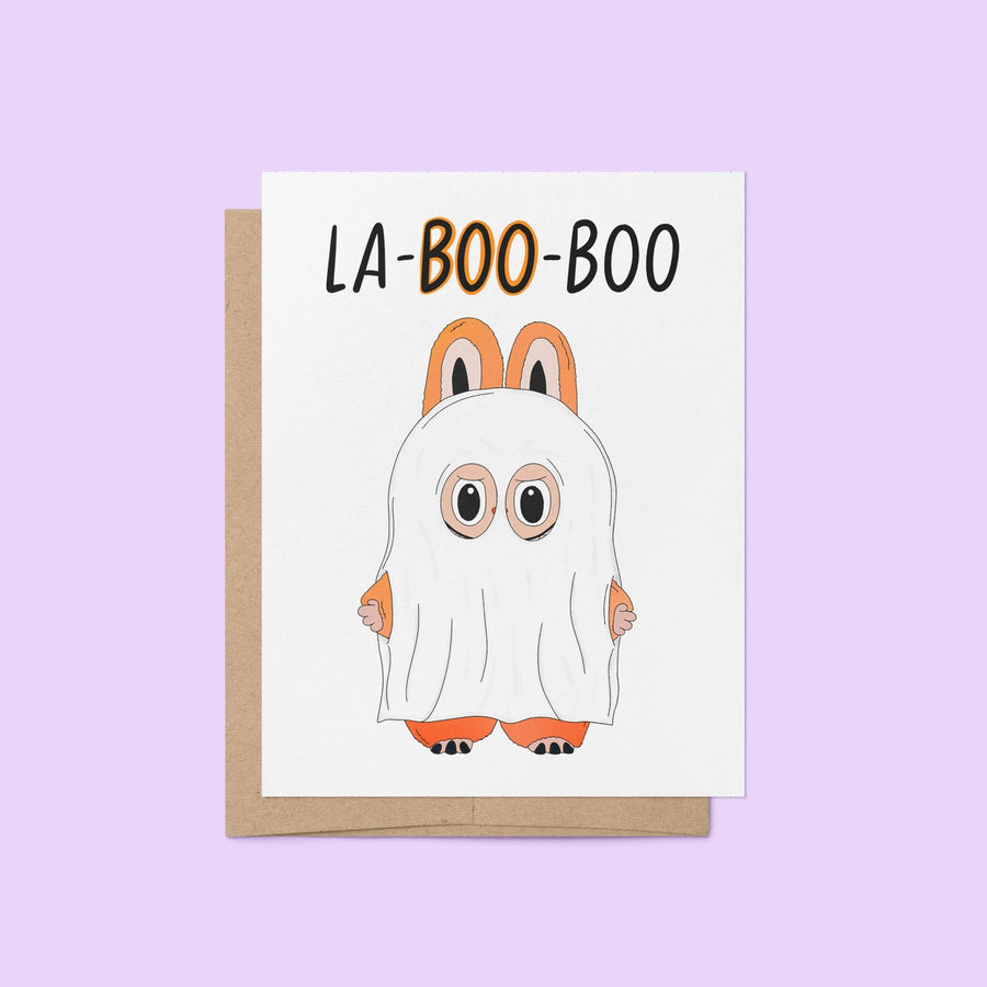 Halloween greeting card with the words “La-BOO-boo” and an illustration of a cute monster in a ghost costume with bunny ears.