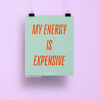 8x10 art print with bold orange glitter-style text reading “My Energy is Expensive” on a mint green background, printed on matte paper and packaged with cardboard backing in a cellophane sleeve.